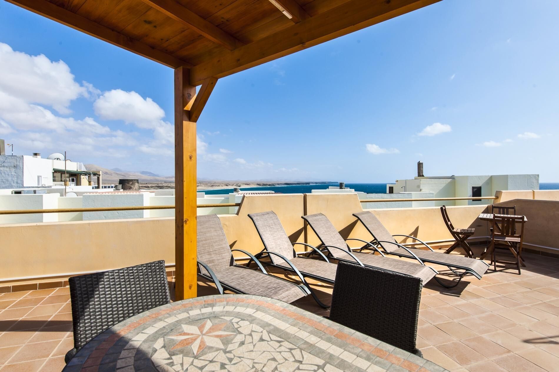 A rooftop terrace with lounge chairs and a table, overlooking a coastal cityscape.