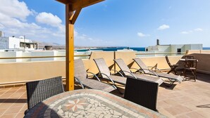 Terraza en la azotea con sillones y una mesa, con vistas a un paisaje urbano costero.