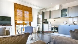 Una cocina moderna con armarios grises, un refrigerador de acero inoxidable y un horno. Hay un comedor con una mesa y sillas, y un televisor sobre un mueble.