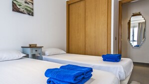 Habitación de hotel con dos camas, un armario de madera, una mesita de noche pequeña y un espejo en la pared.