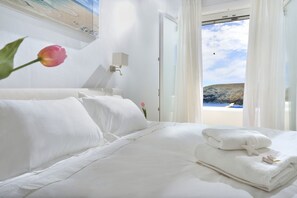 Une chambre d’hôtel avec un lit, du linge de lit blanc, une table de chevet, une lampe et une vue sur la plage.