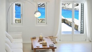 Une pièce avec un canapé blanc, une table en bois ornée de bougies et une vue sur une mer bleue, visible à travers de grandes fenêtres.