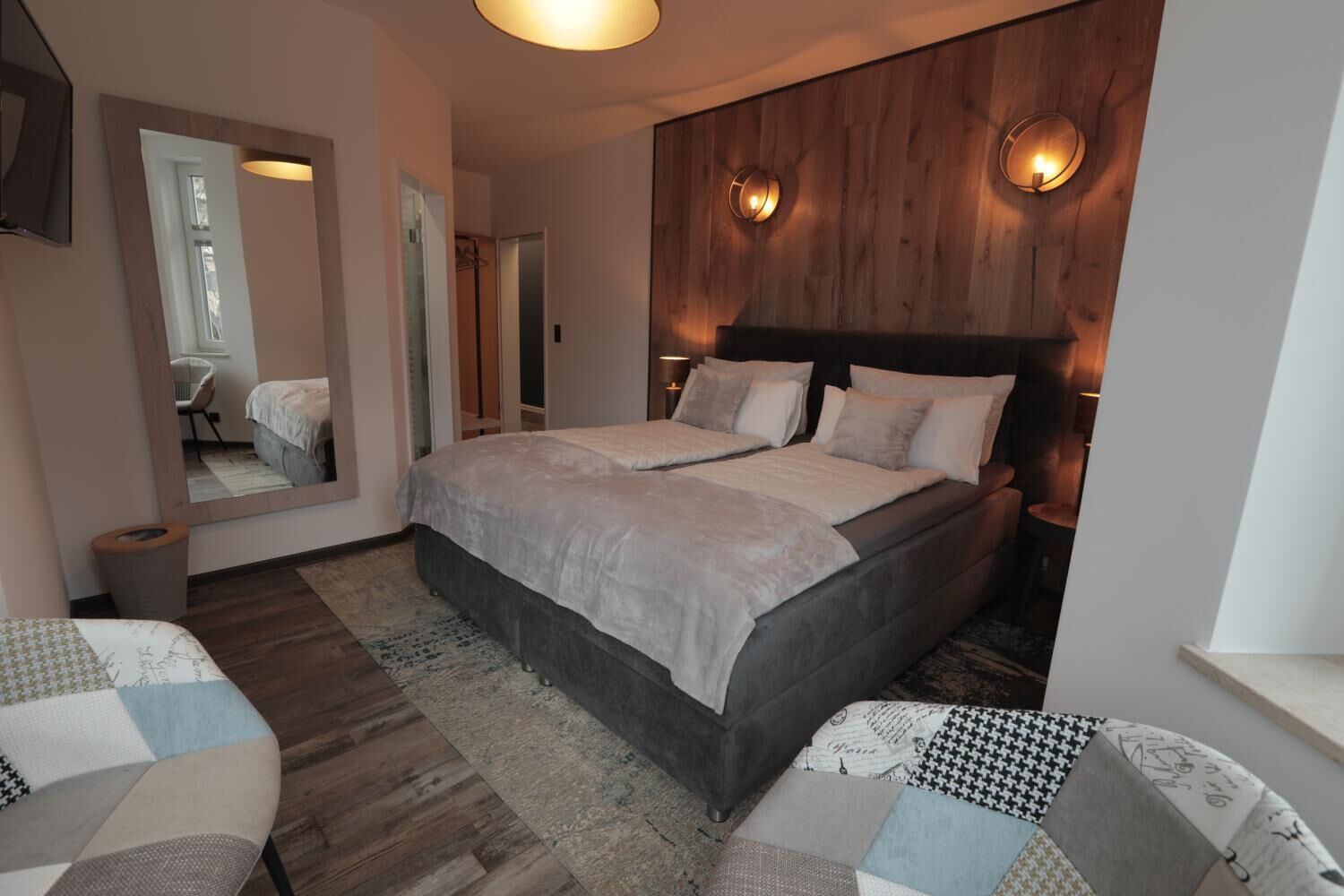 A modern bedroom with a large bed, a wooden accent wall, and a mirror.