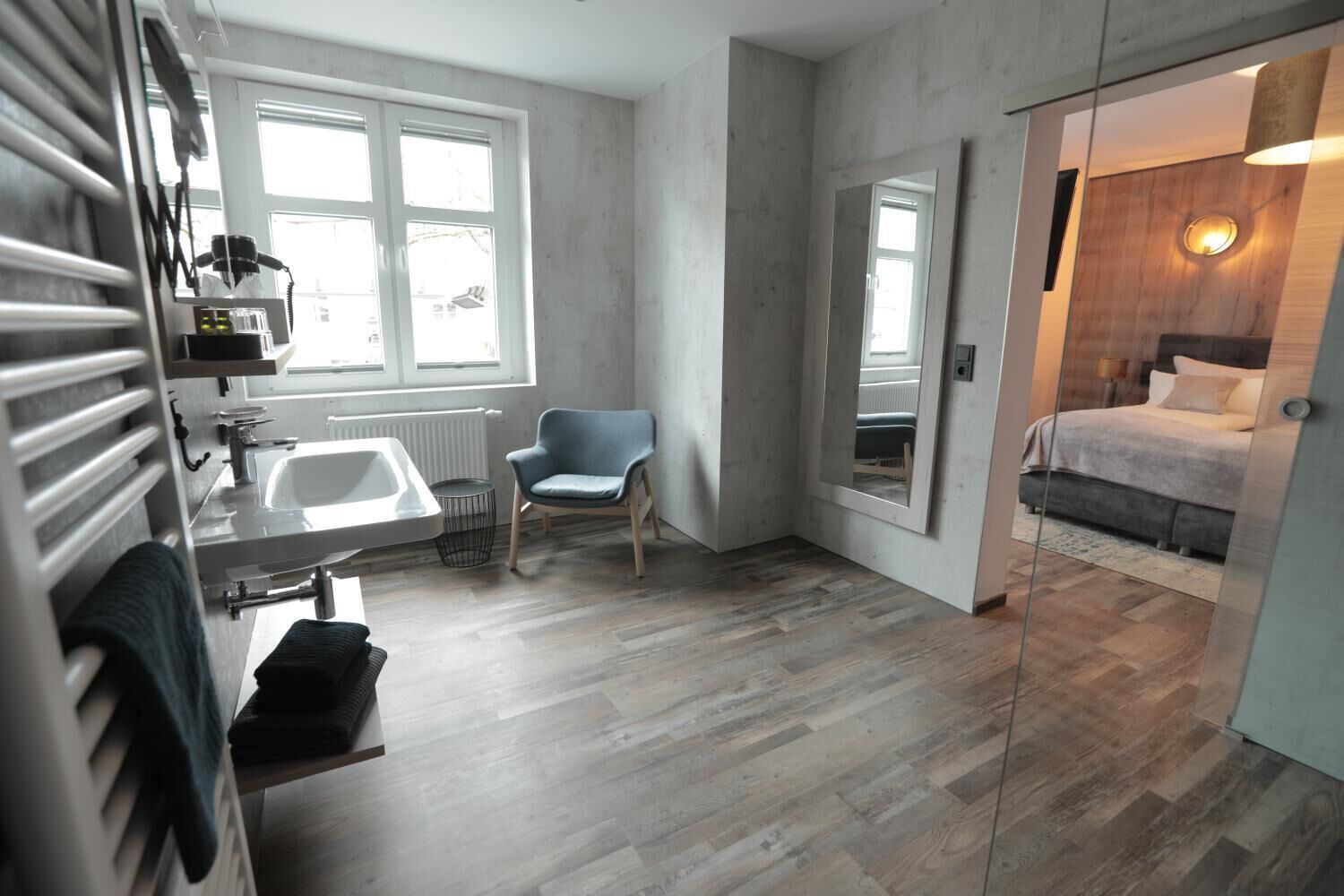 Een moderne badkamer met een badkuip, een wastafel en een stoel. Er is een groot raam en een spiegel aan de muur.