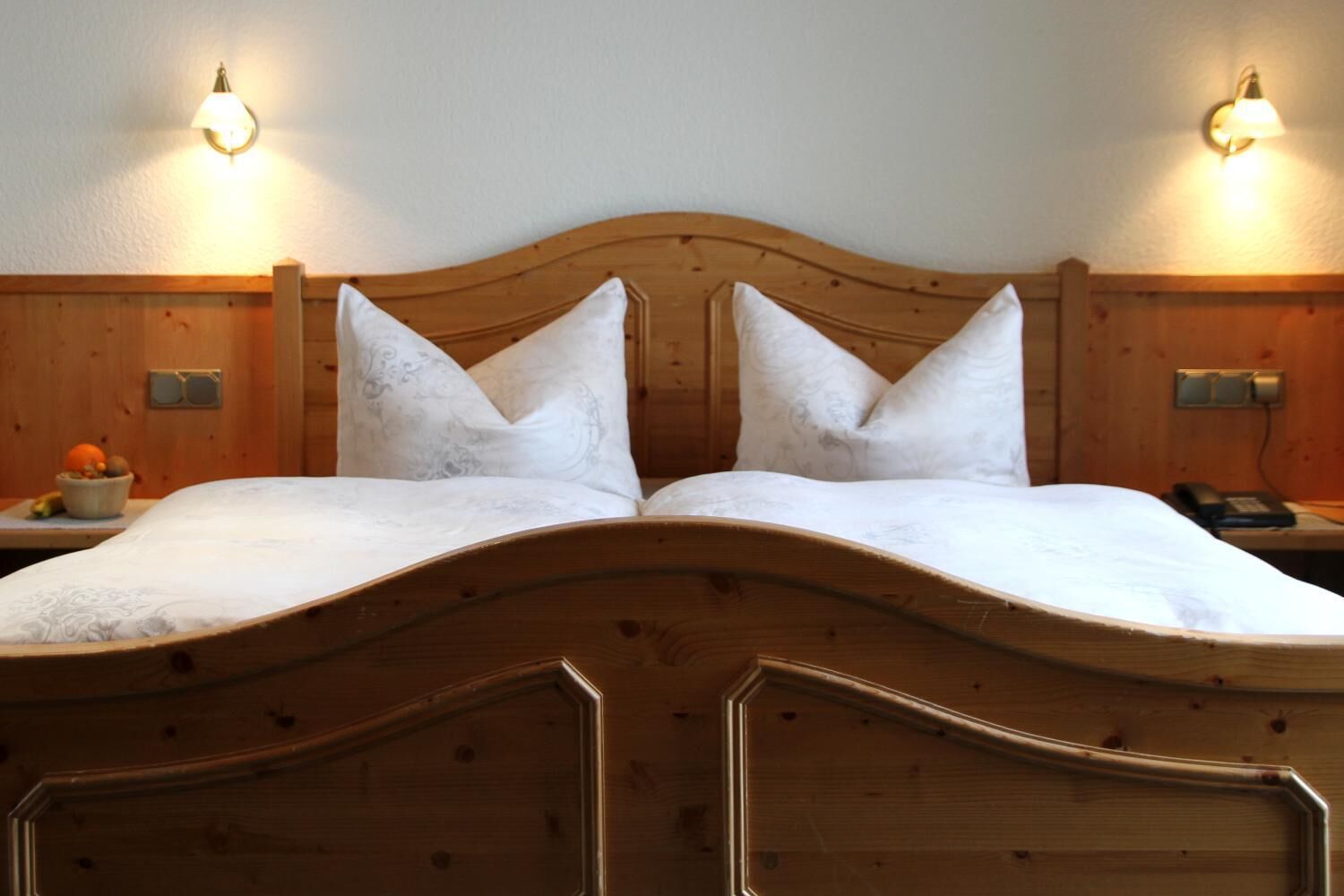 A double bed with a wooden headboard, two bedside tables with lamps, and a fruit bowl on the left side.
