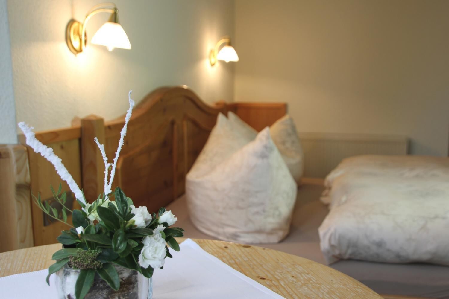 Una camera d'hotel con una testiera in legno, due lampade a parete, un letto con biancheria da letto bianca e un piccolo vaso con una pianta sul comodino.