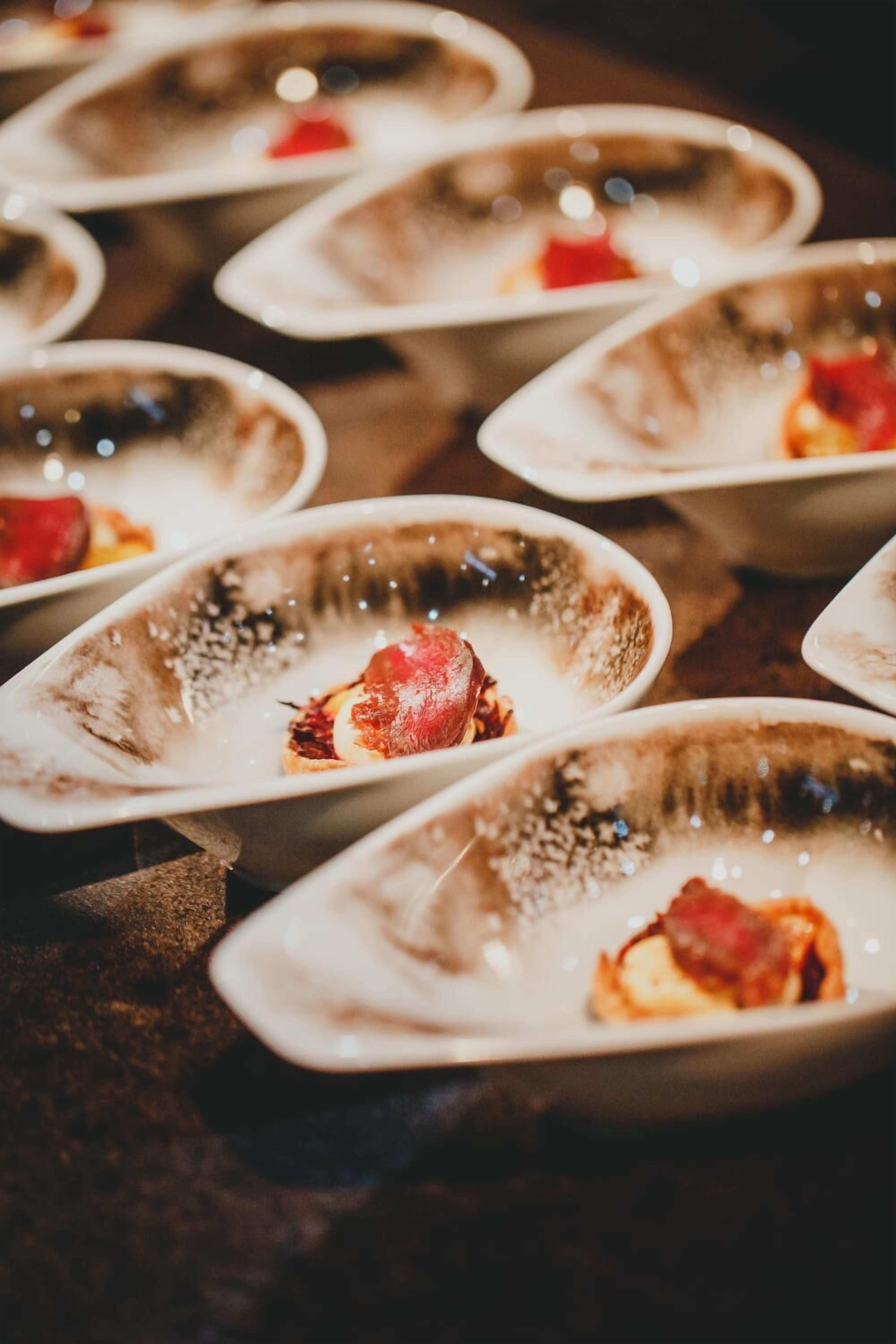 A series of oval-shaped dishes with a darkened center, possibly containing food, arranged on a dark surface.