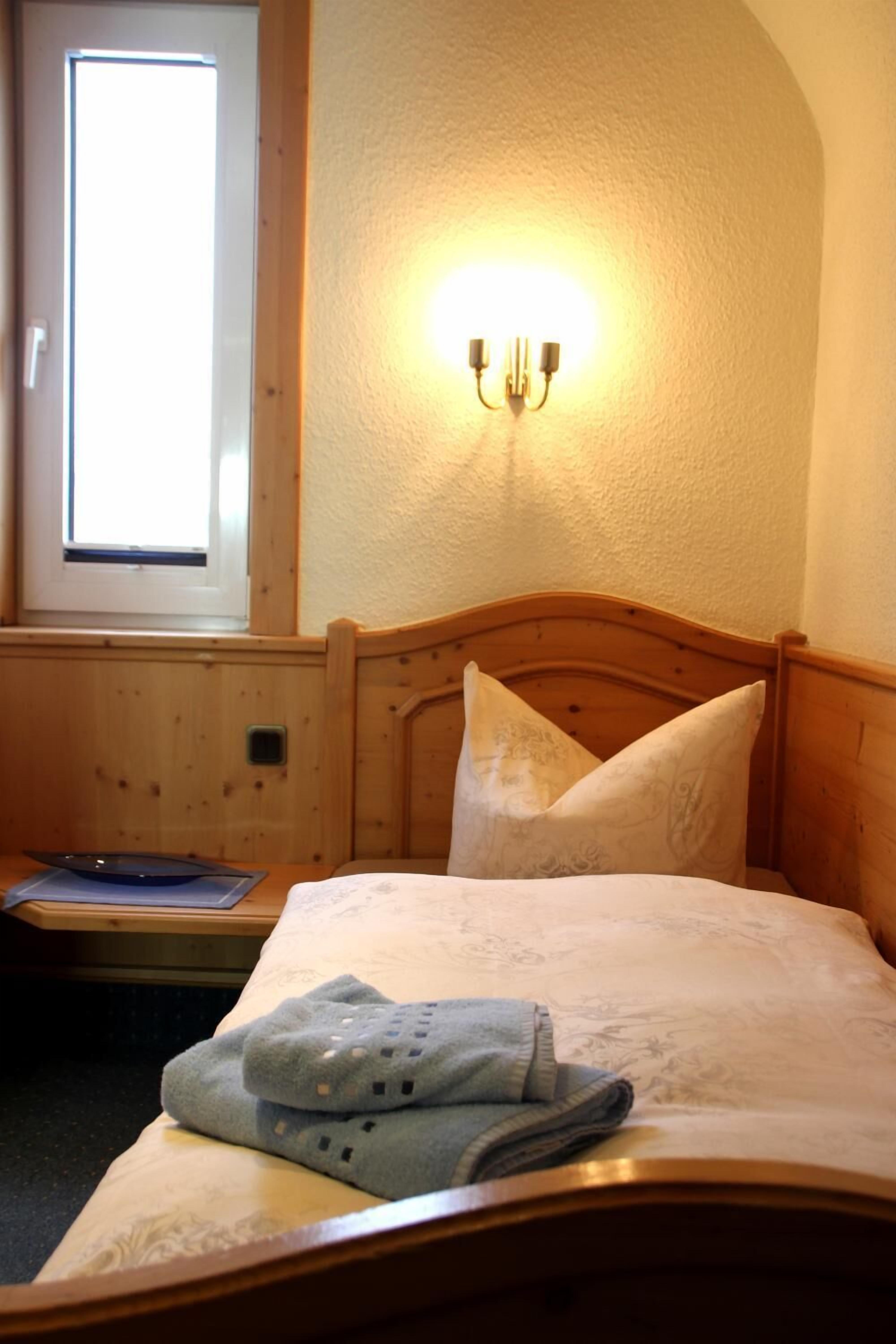 Un dormitorio con cabecera de madera, mesita de noche, lámpara y ventana con luz natural.