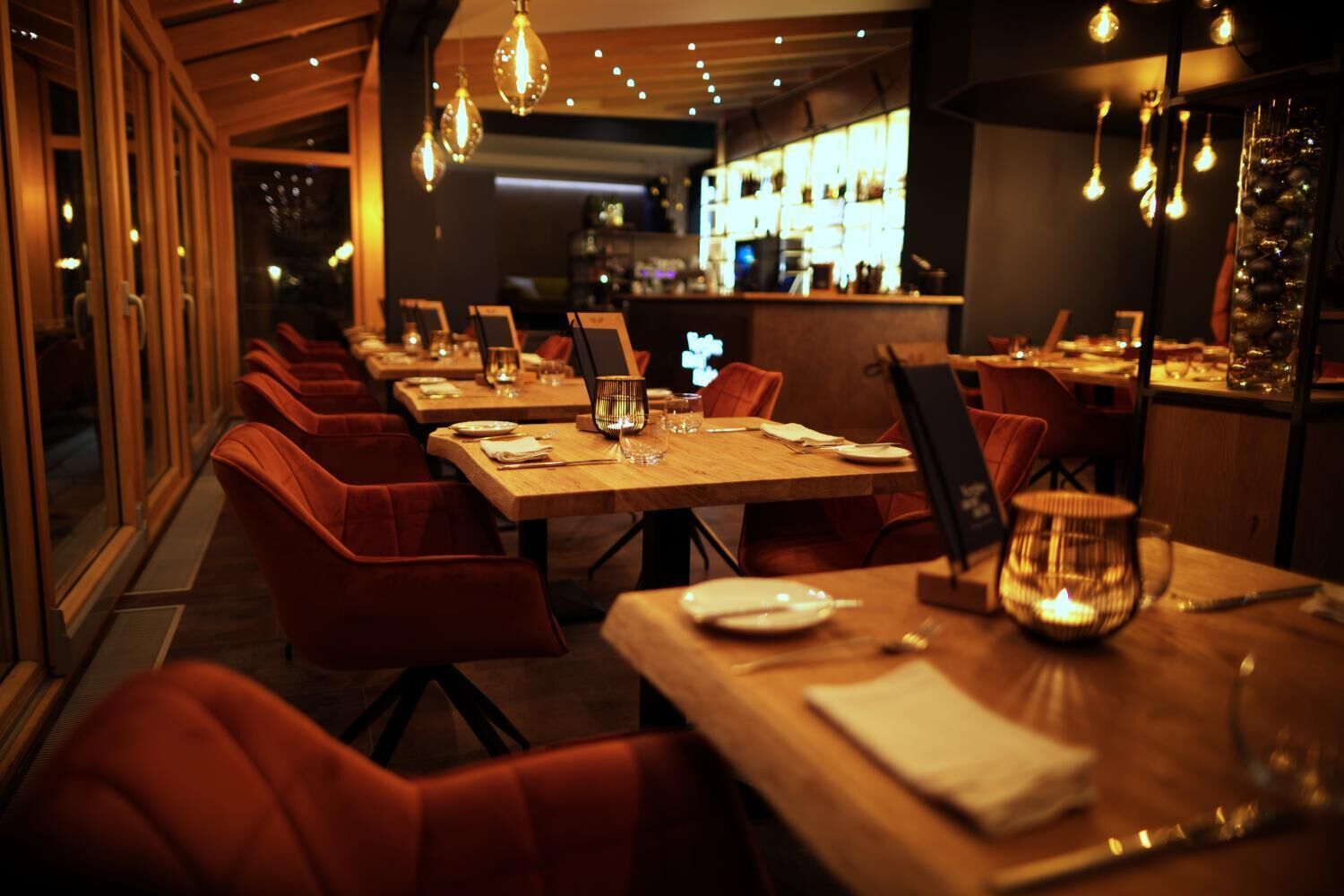 A restaurant with wooden tables and red chairs, lit by hanging lamps.