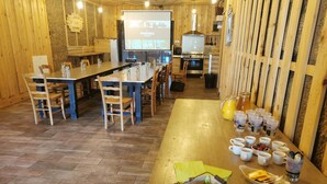 A cozy breakfast area with wooden tables and chairs, a projection screen displaying 'PUISSANCE', and a kitchen area with a stove and sink. - Le Moulin de la Fortie (Viscomtat)