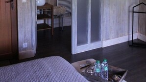 A rustic room with wooden walls, a bed, a small table with bottles, and a hanging coat rack. - Le Moulin de la Fortie (Viscomtat)