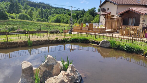 A rustic house with a stone facade and a tiled roof, surrounded by a wooden fence and a small pond with rocks and plants. - Le Moulin de la Fortie (Viscomtat)
