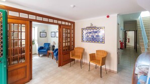 Amplia sala de estar con una puerta de madera, dos sillones de mimbre, un sofá azul y piso de baldosas.