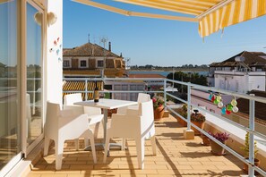 A balcony with white chairs and a table, potted plants, and a view of buildings and the sea. - Villa Marquez (Vila Real Santo Antonio)