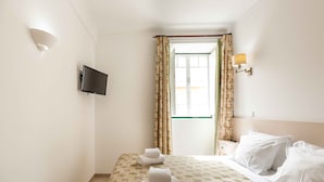 Habitación de hotel con cama, televisión de pantalla plana en la pared, lámpara de noche y ventana con cortinas.