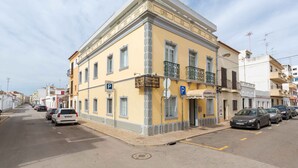 Un edificio amarillo con balcón, un letrero de estacionamiento y varios coches aparcados.