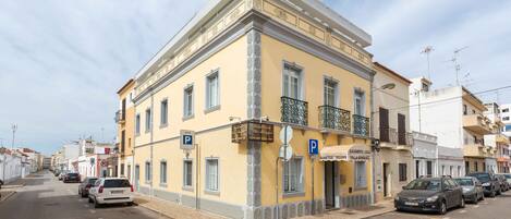 A yellow building with a balcony, a parking sign, and several parked cars.