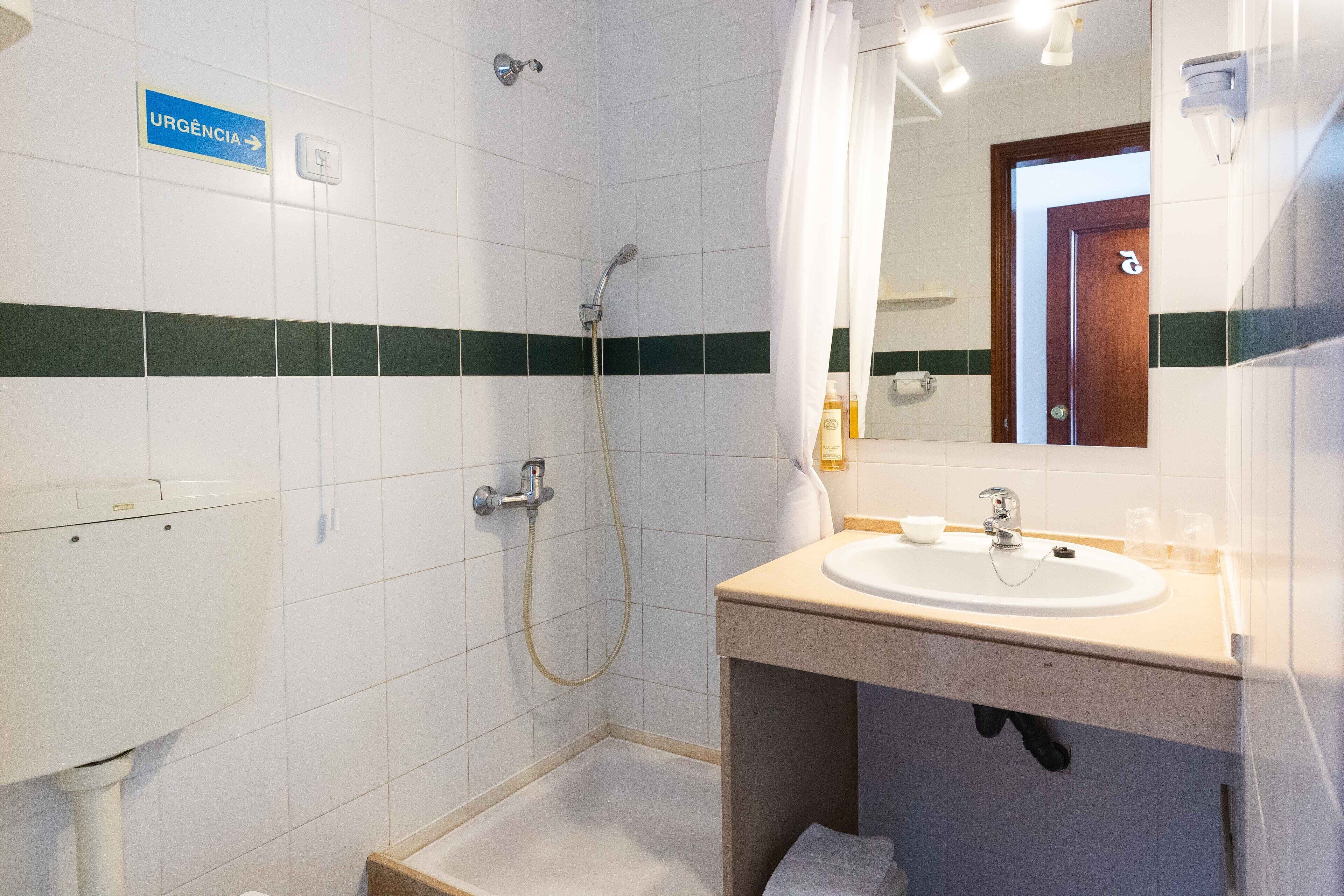 Baño con ducha, lavamanos y un letrero que indica una salida de emergencia.