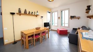 A dining area with a wooden table and chairs, a television, and a red ottoman.