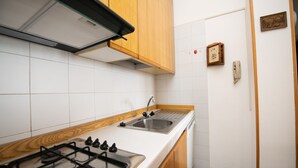 A kitchen with white tiles, wooden cabinets, a stainless steel sink, and a gas stove.