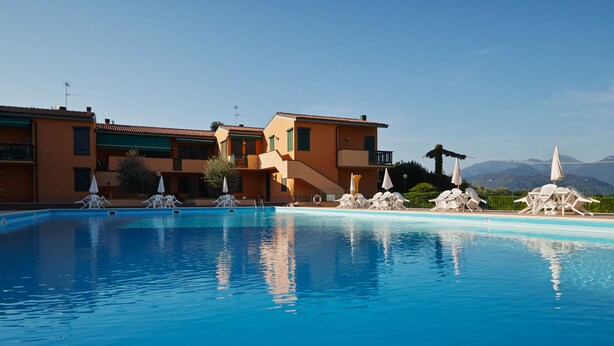 A swimming pool with lounge chairs and umbrellas, surrounded by multi-story buildings with balconies.