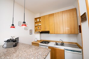 A compact kitchen with wooden cabinets, a granite countertop, a gas stove, a dishwasher, and two pendant lights.