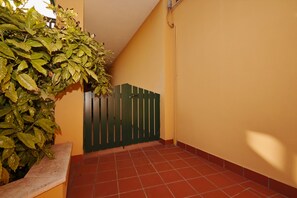 A hallway with a green gate, a potted plant, and red-tiled flooring.