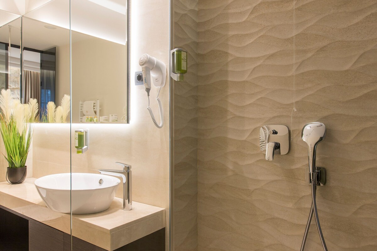 Un baño moderno con cabina de ducha de vidrio, un lavabo blanco con espejo y un secador de pelo montado en la pared.