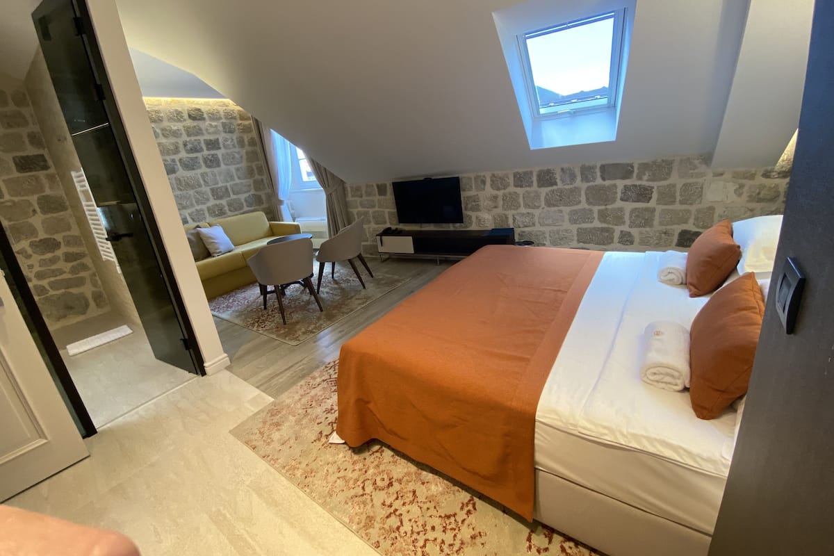 Un dormitorio con una cama, televisión, pared de piedra y ventana.