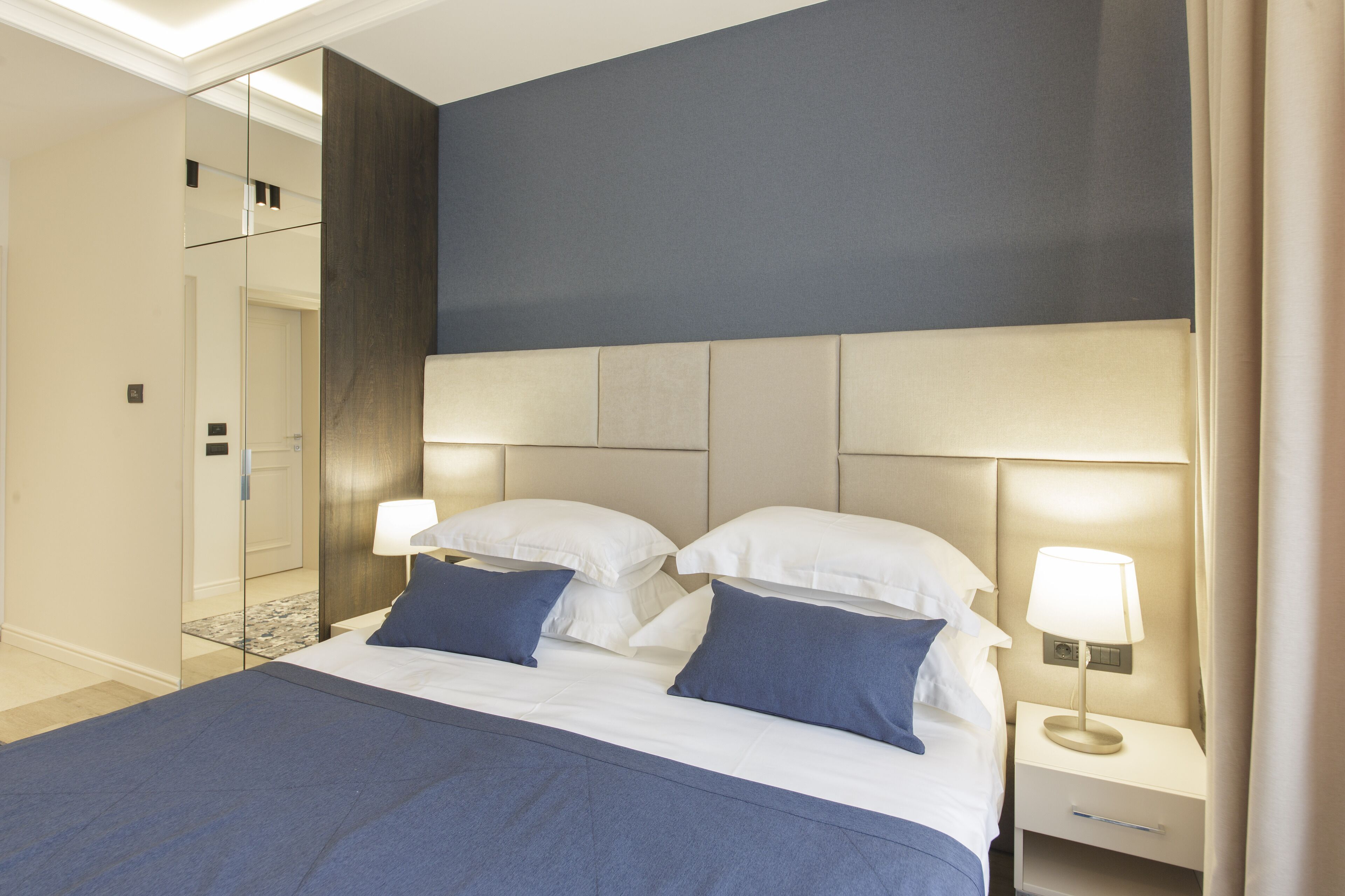 A hotel room with a large bed, two bedside tables, a mirror, and a nightstand with a lamp.
