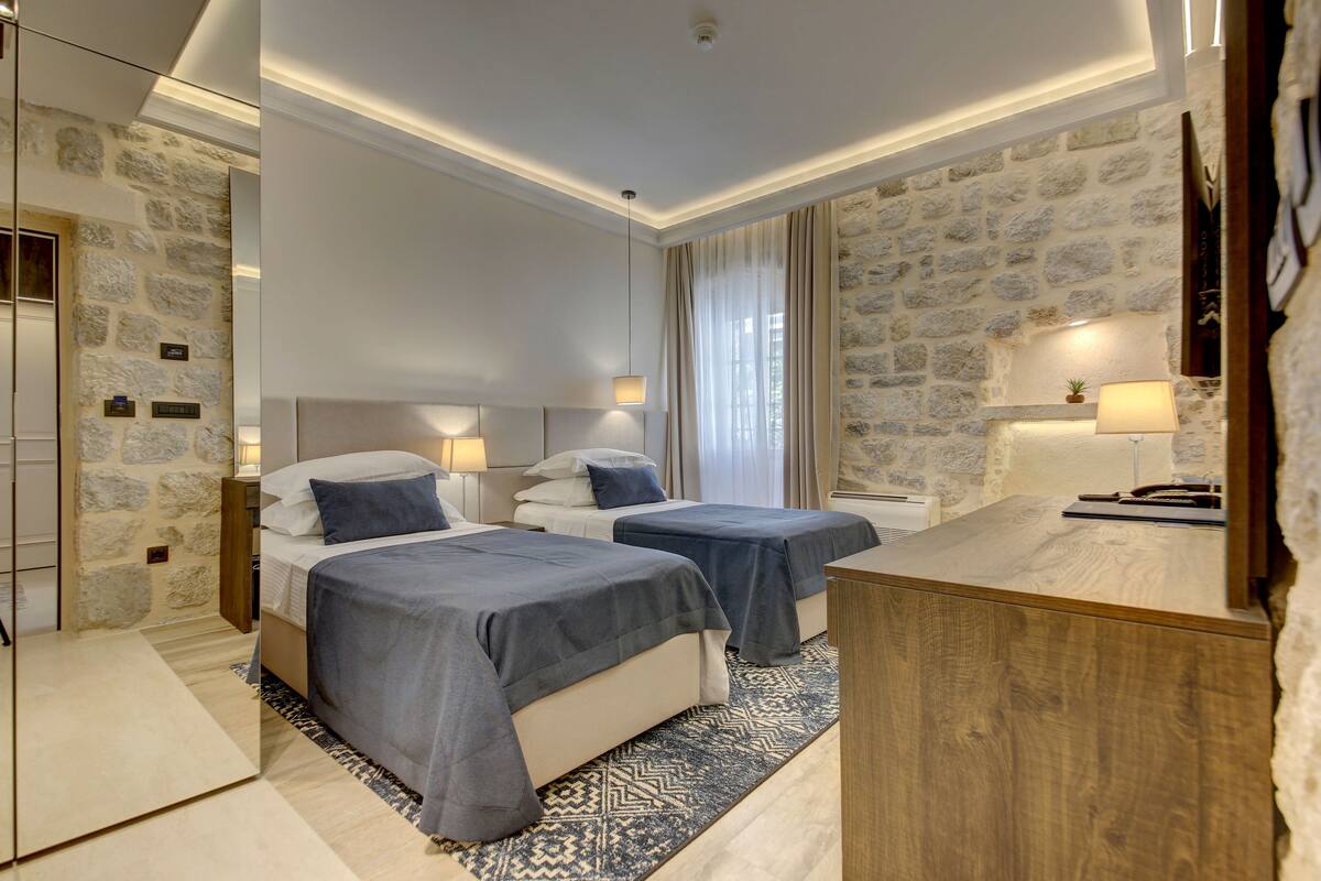 Una habitación de hotel con dos camas, un escritorio de madera, paredes de piedra y un espejo grande.