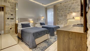 Una habitación de hotel con dos camas, un escritorio de madera, paredes de piedra y un espejo grande.