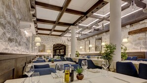 Un restaurante con mesas blancas, sillas azules y paredes de piedra.