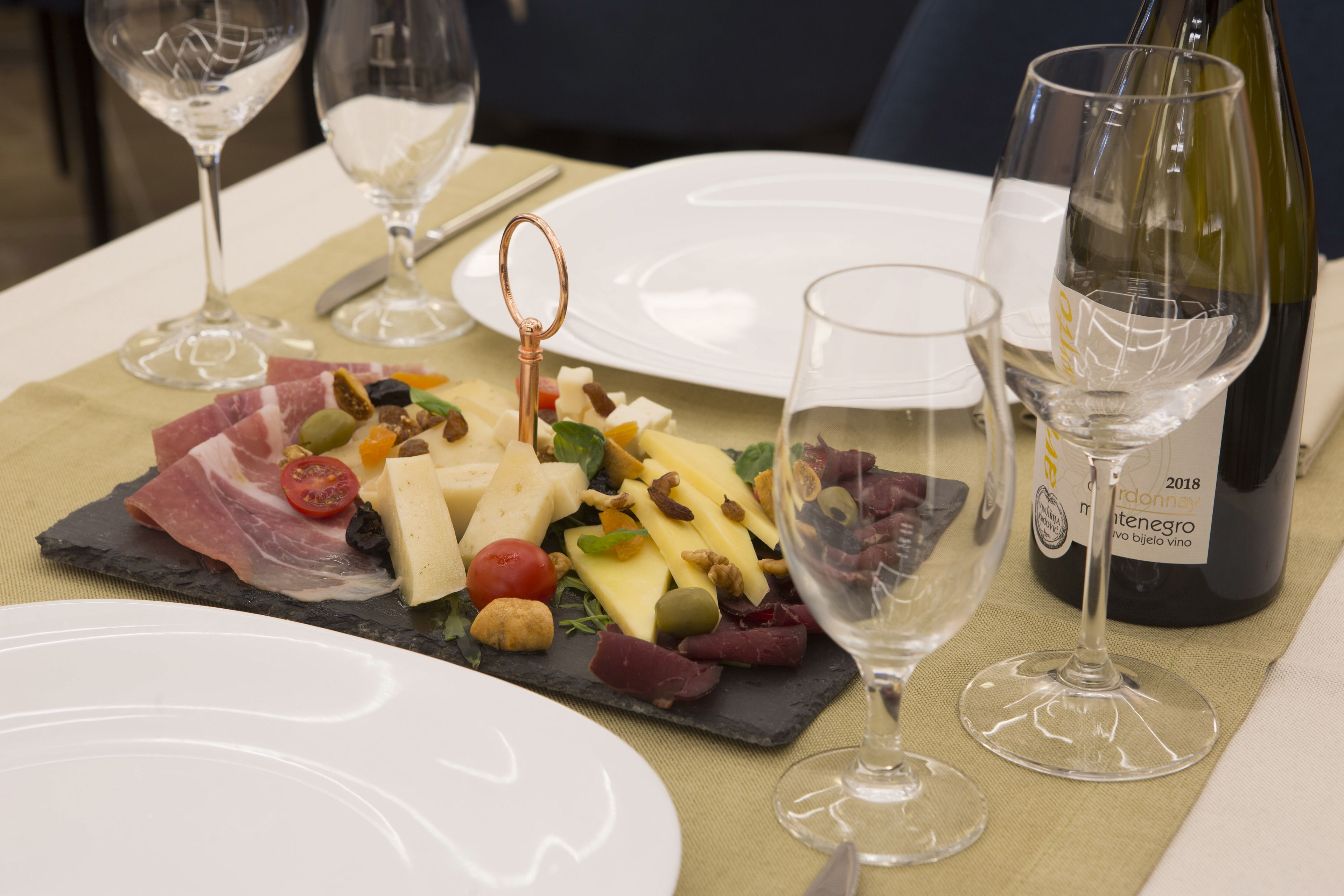 Una mesa de comedor con una tabla de quesos y embutidos, copas de vino y una botella de vino.