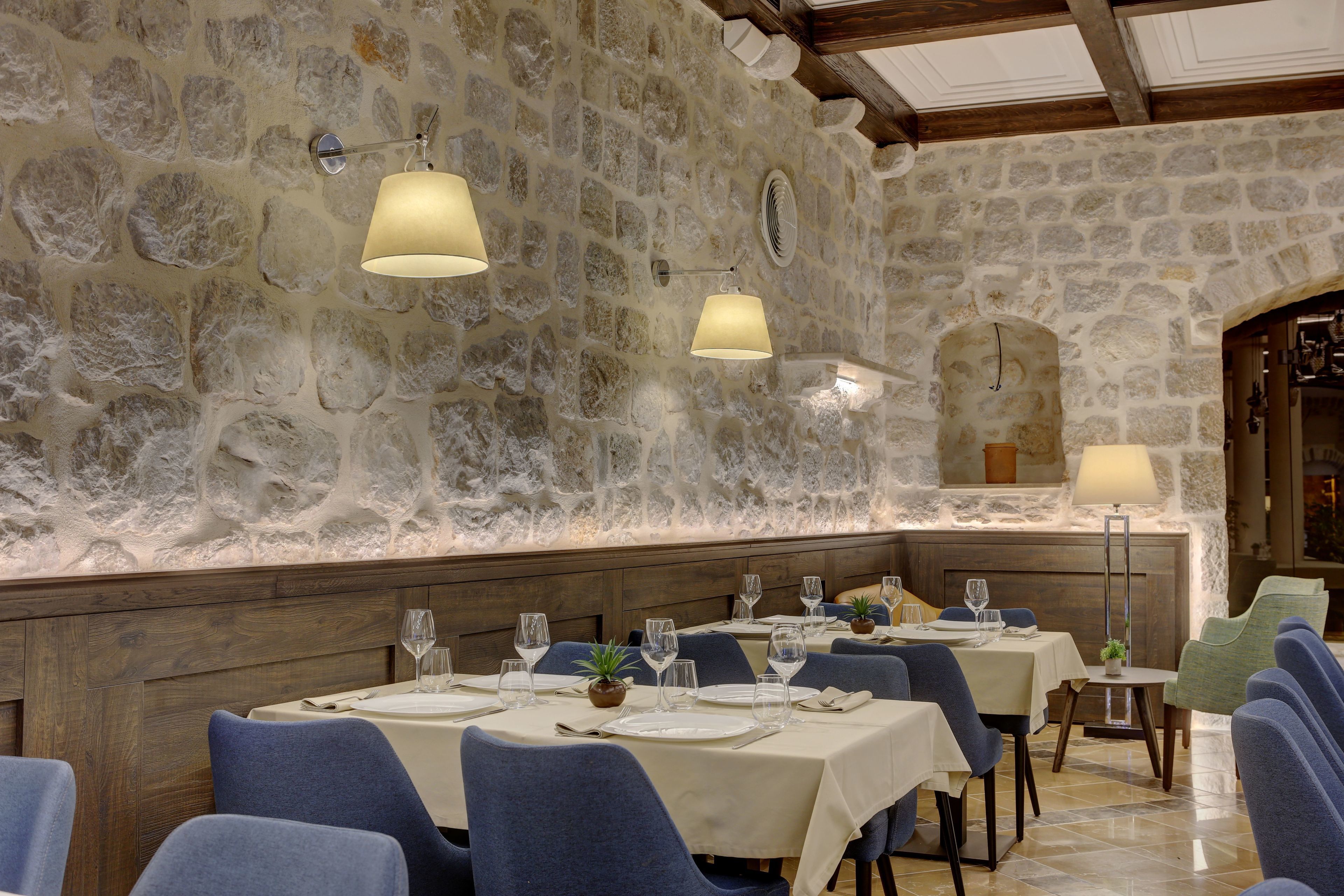 Een restaurant met stenen muren, blauwe bekleden stoelen en tafels gedekt met wijnglazen en borden.