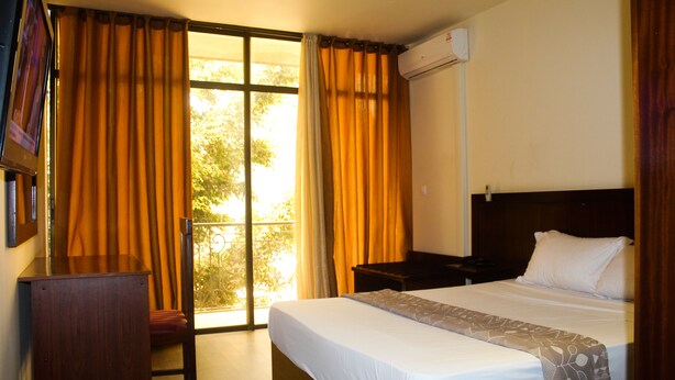 A hotel room with a bed, a desk, a chair, and a window with curtains. - Sacha Hotel (Conakry)