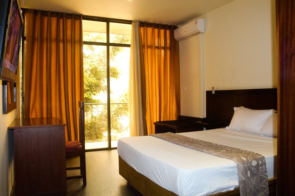 Una habitación de hotel con cama, escritorio, silla y ventana con cortinas.