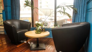 A room with two black armchairs, a small round table with a vase of flowers, and a view of the street through large windows. - Sacha Hotel (Conakry)