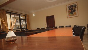 A conference room with a long table, chairs, a wooden door, and a window with curtains. - Sacha Hotel (Conakry)