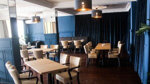 A restaurant with wooden tables and chairs, dark blue walls, and hanging pendant lights. - Sacha Hotel (Conakry)