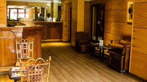 A lobby with wooden flooring, a reception desk, and leather armchairs. - Sacha Hotel (Conakry)