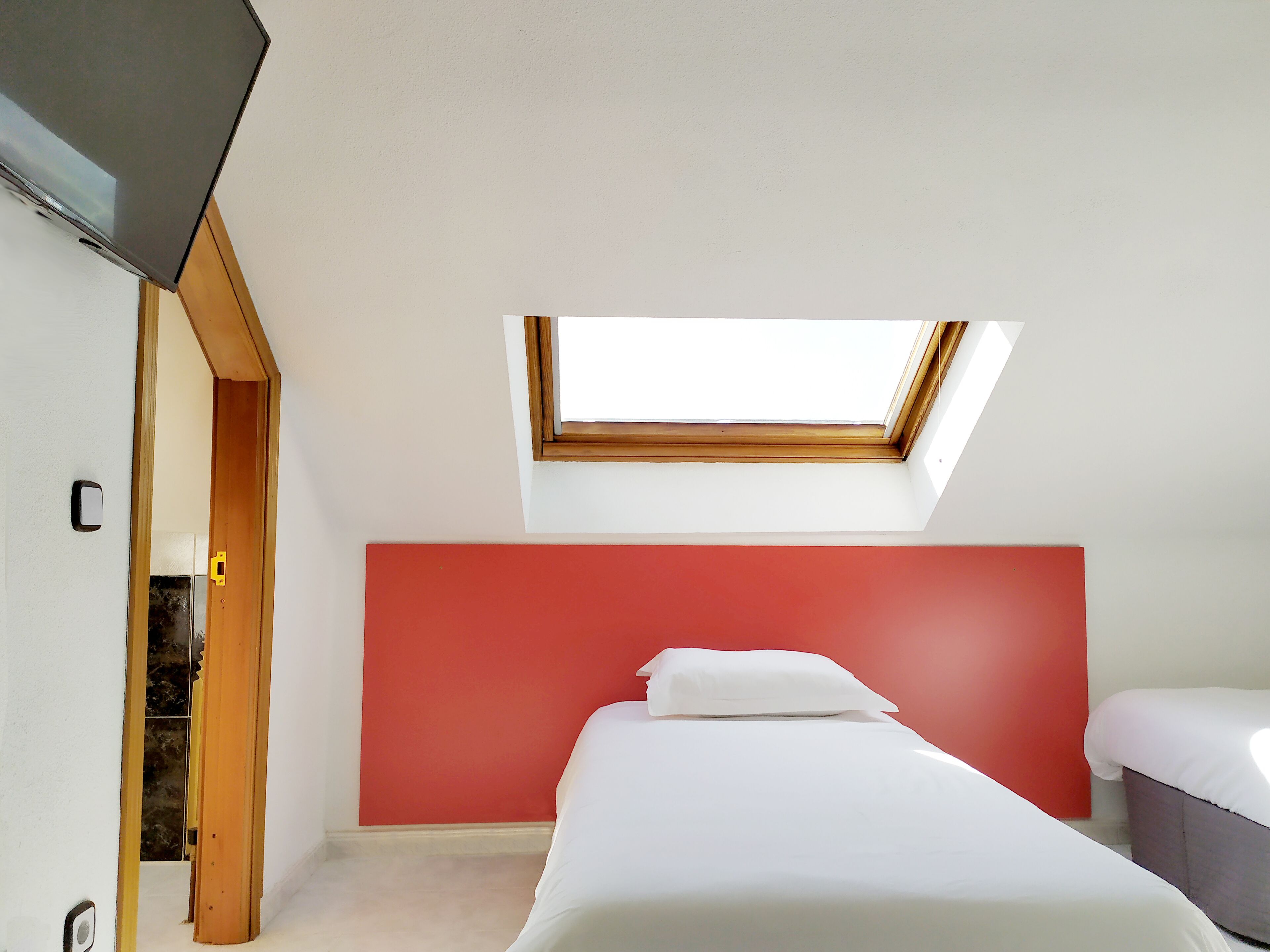 A bedroom with a skylight, a red accent wall, and a bed with white bedding.