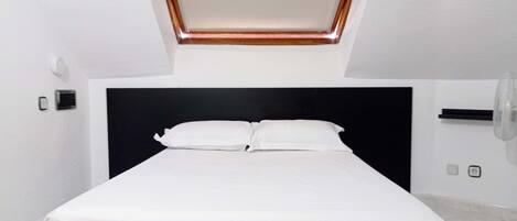 A modern bedroom with a skylight, a black headboard, and a white bedspread.