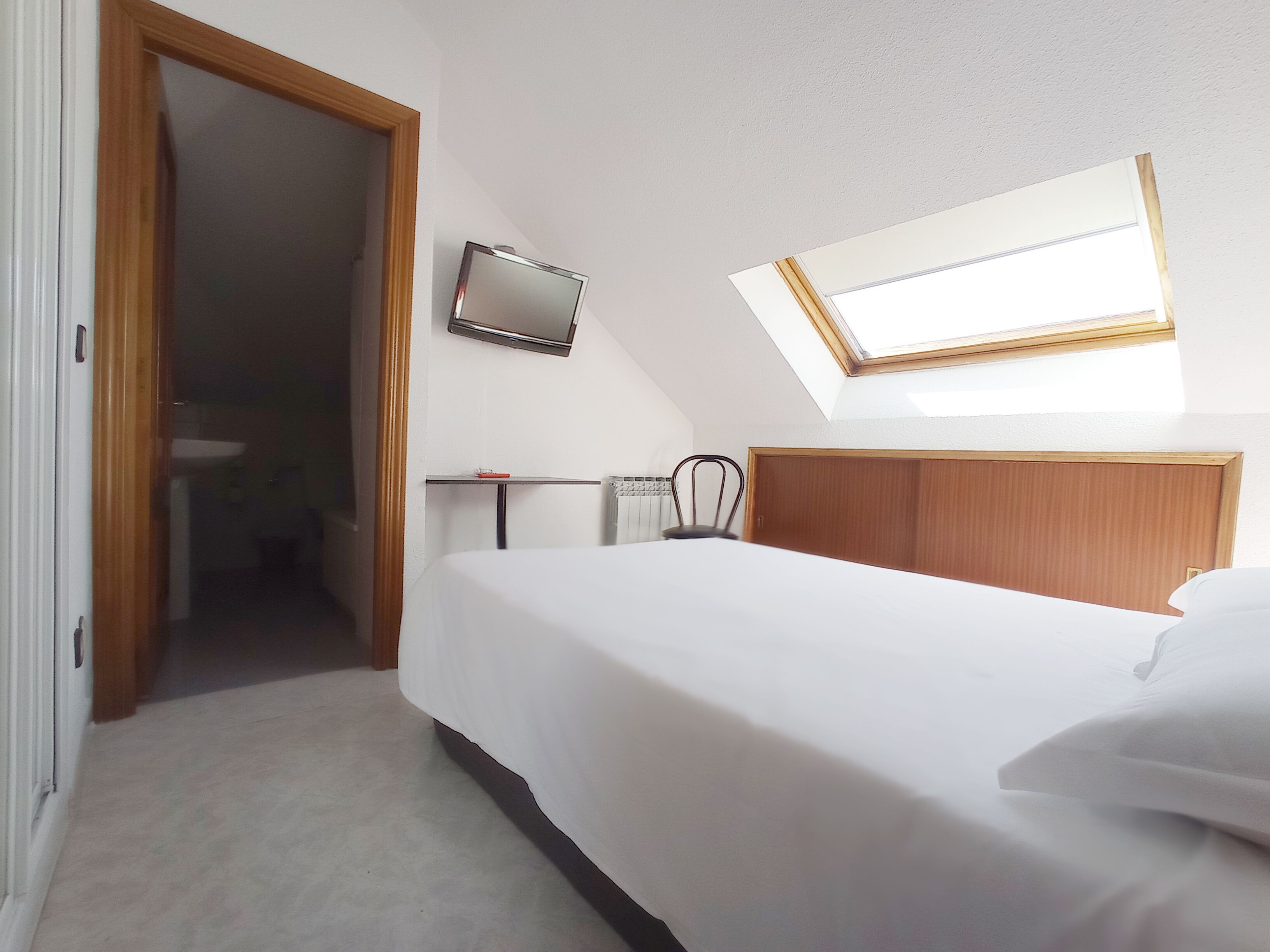 Ein Hotelzimmer mit Bett, Nachttisch, Stuhl, Fernseher, Fenster und Tür.