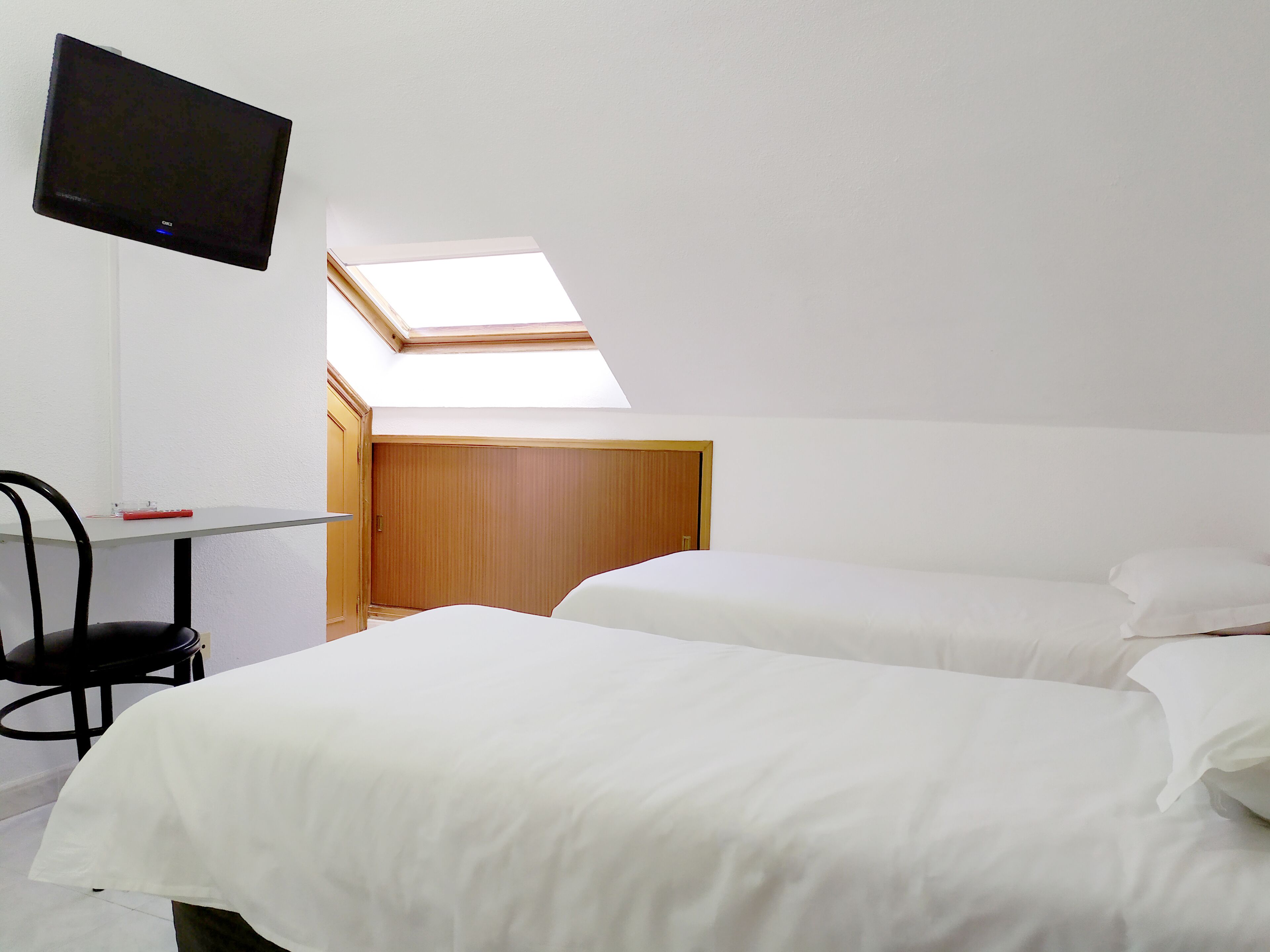 A room with two beds, a desk, a chair, a TV, and a skylight.