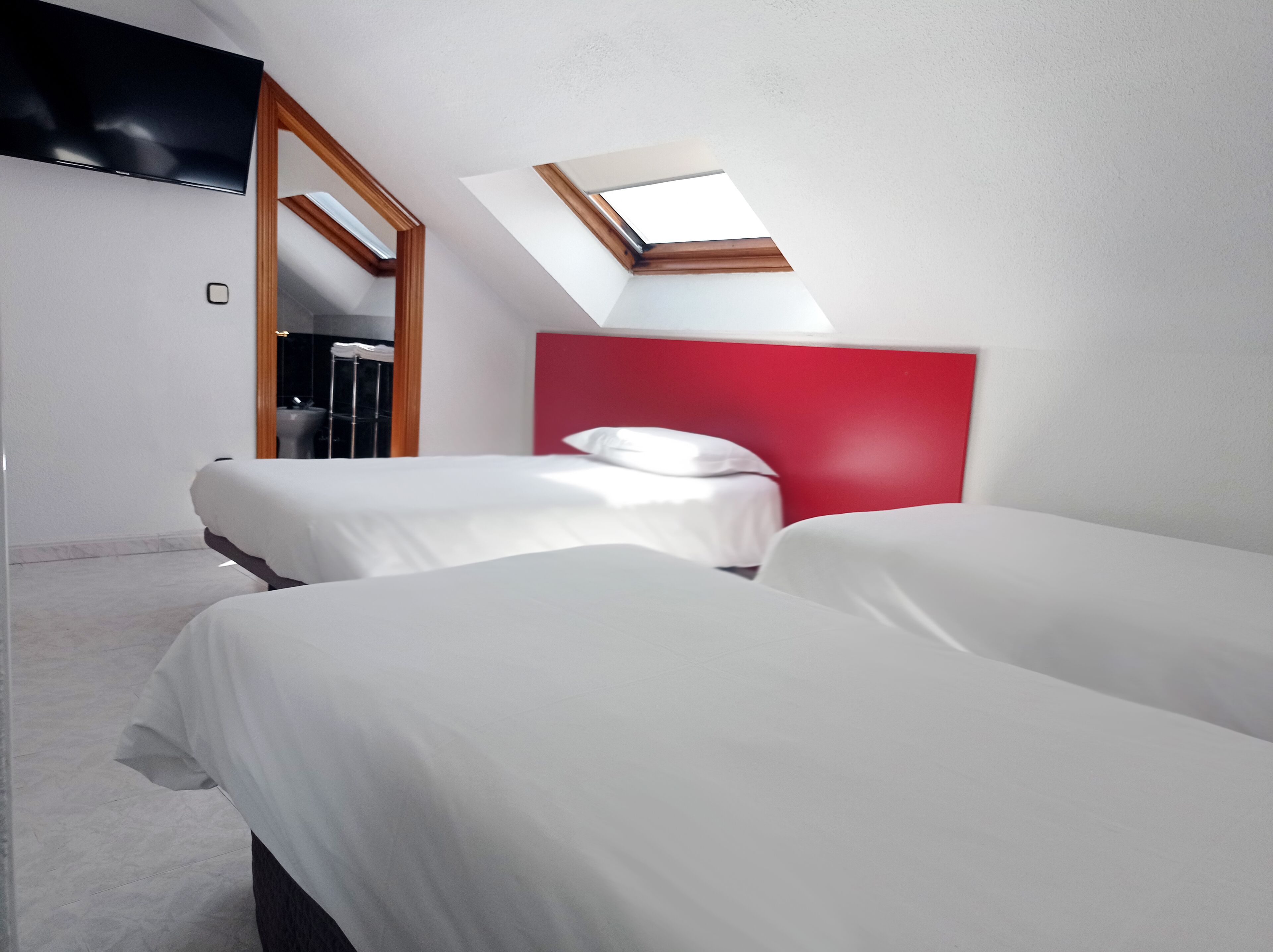 Hotellihuone, jossa on kaksi sänkyä, punainen pääty, kattovalokuvio ja seinälle asennettu televisio.