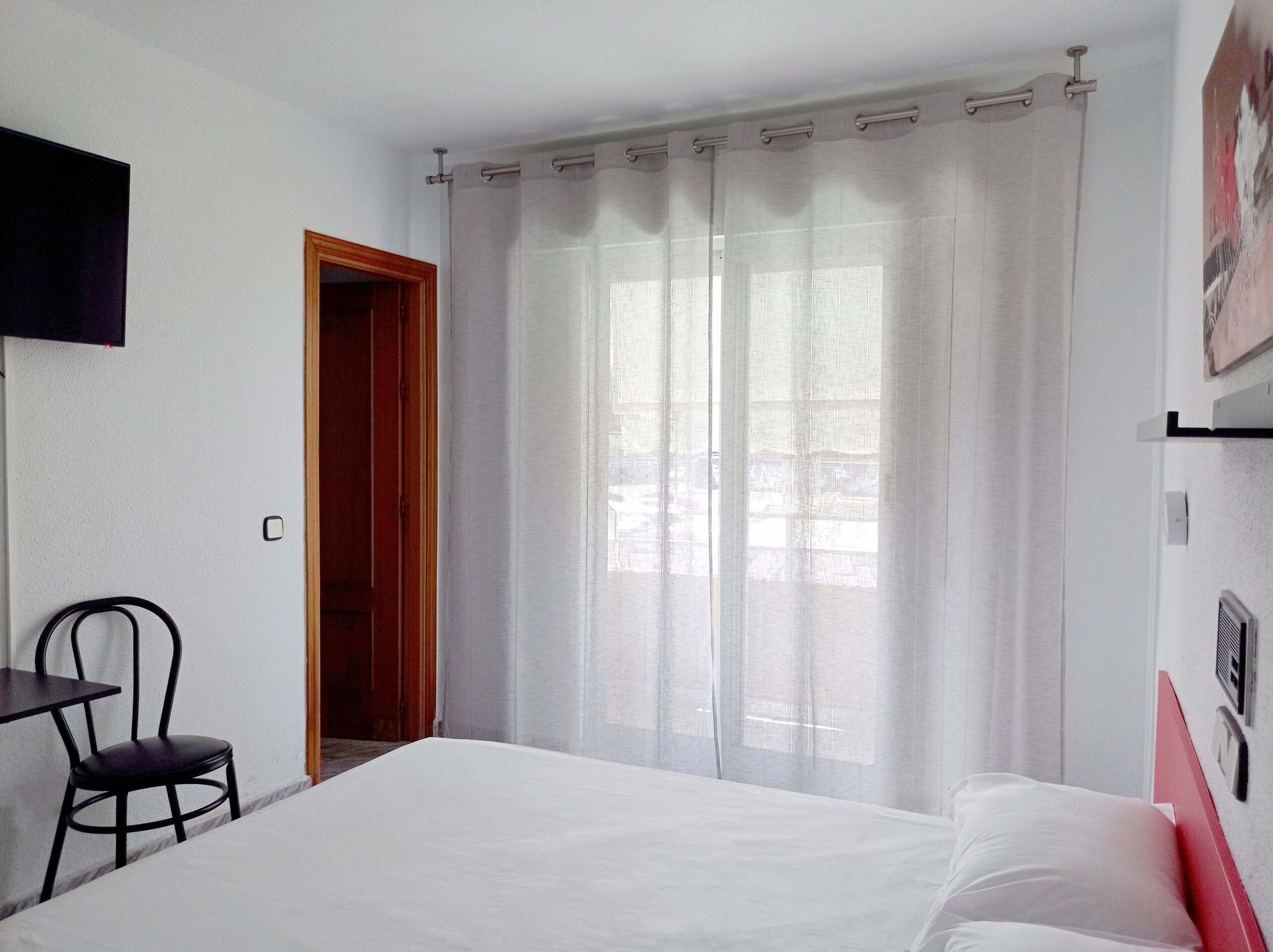 Ett hotellrum med en säng, en stol, ett skrivbord och ett fönster med gardiner.