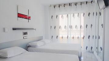 Quarto de hotel com duas camas, televisão montada na parede, janela com cortinas decorativas e unidade de ar condicionado também fixada na parede.