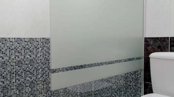 A modern bathroom with a glass shower enclosure, a toilet, and mosaic tile walls.