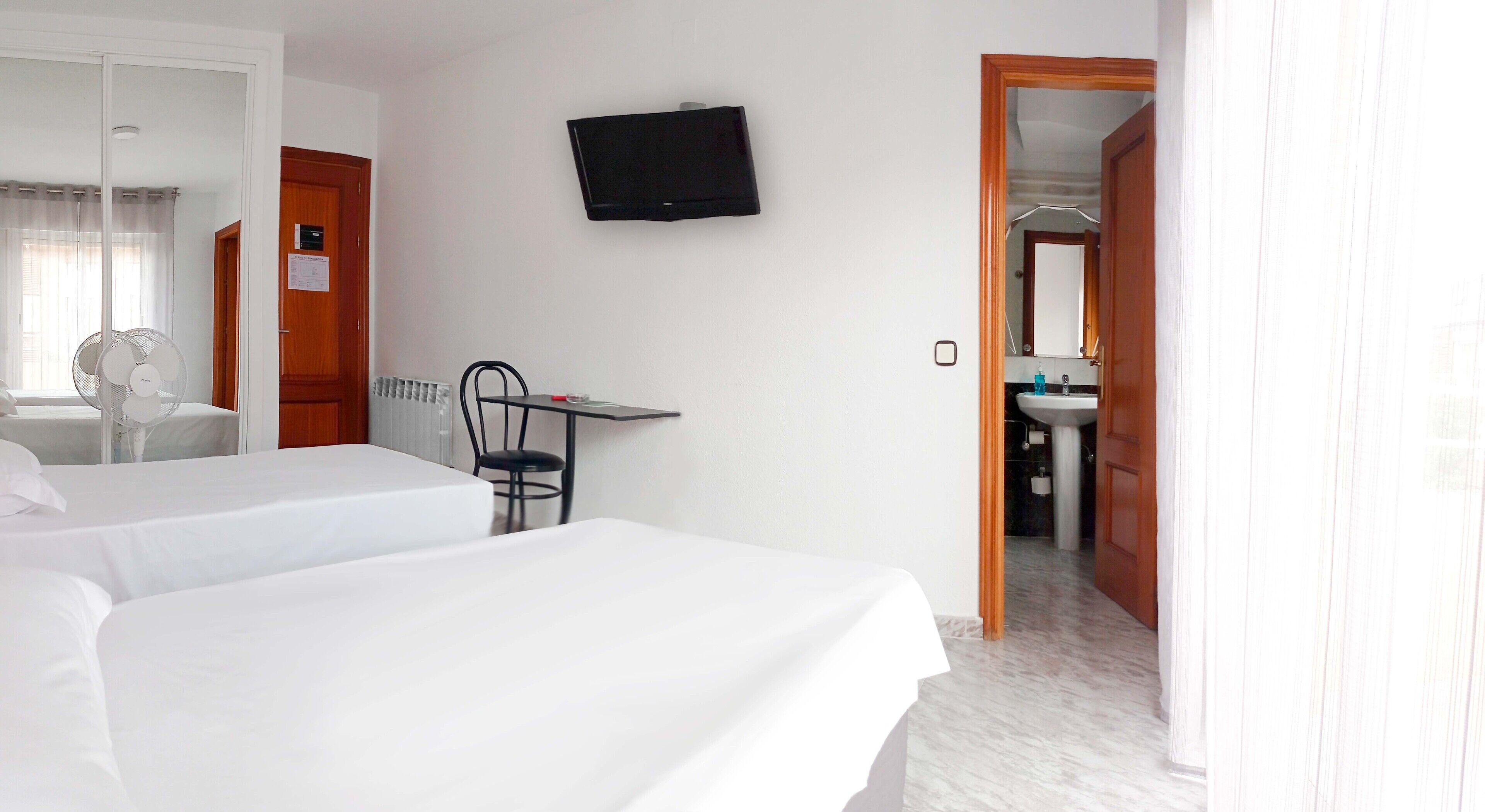 A hotel room with two beds, a desk, a chair, a TV, and a bathroom visible through an open door.